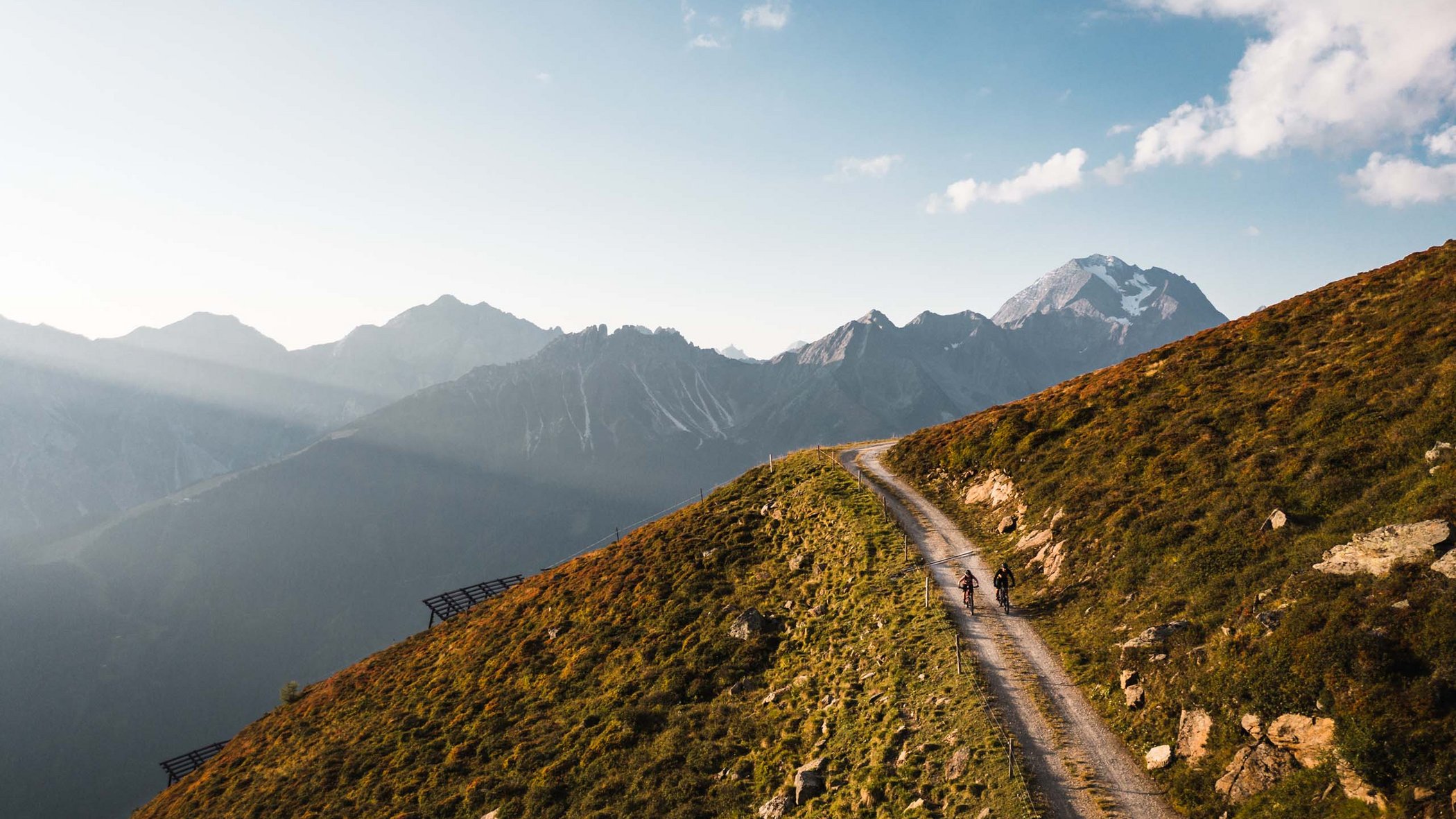 Stubaital: activities in summer Two cyclists on mountain trail with Alps and blue sky in the background